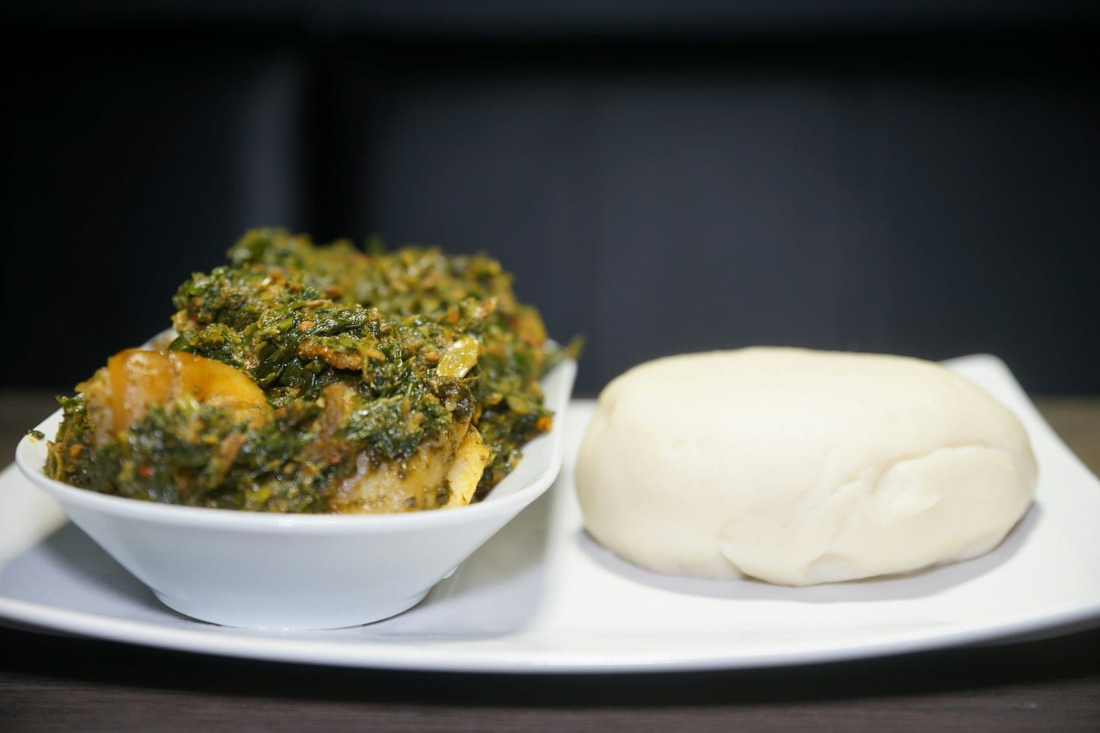 A ball of white swallow beside a bowl of efo riro vegetable soup