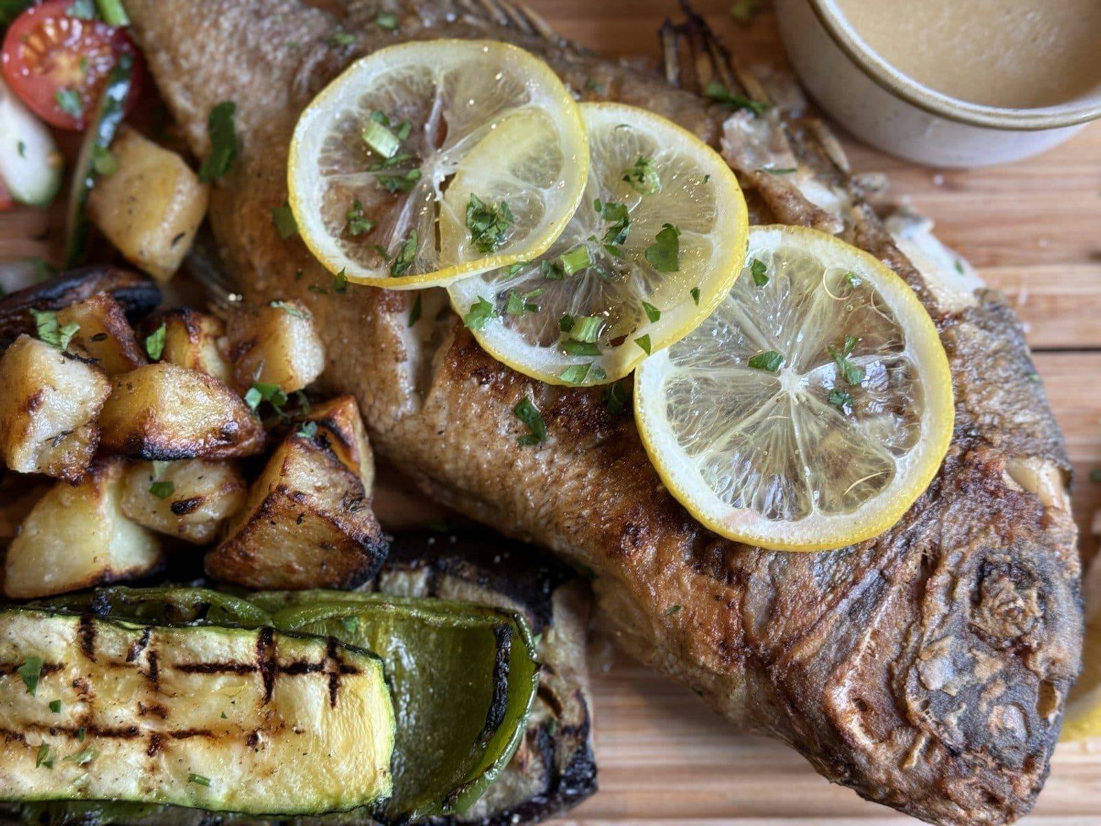A whole roasted fish with lemon slices, roast potatoes and grilled vegetables